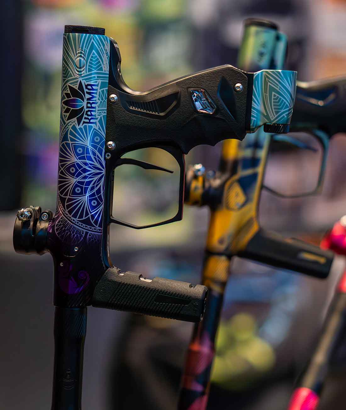 Zwei bunt bedruckte Paintballmarkierer stehen in einem Ständer
